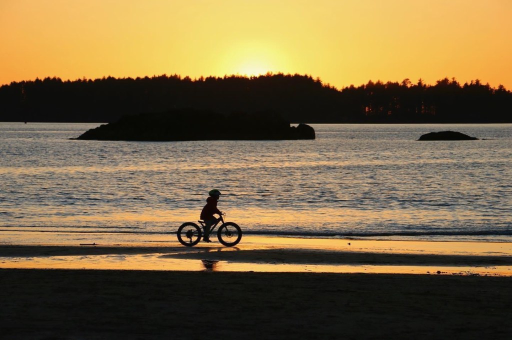 A kid rides their bike on Mackenzie beach in Tofino at sunset